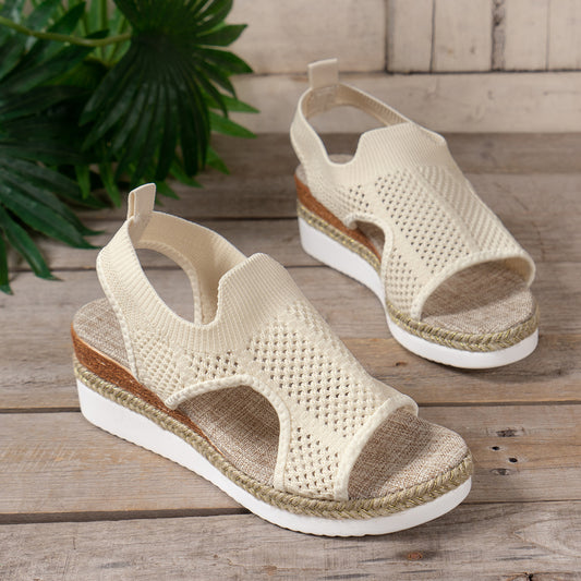 Beige sandals with woven design on a wooden surface with greenery in the background
